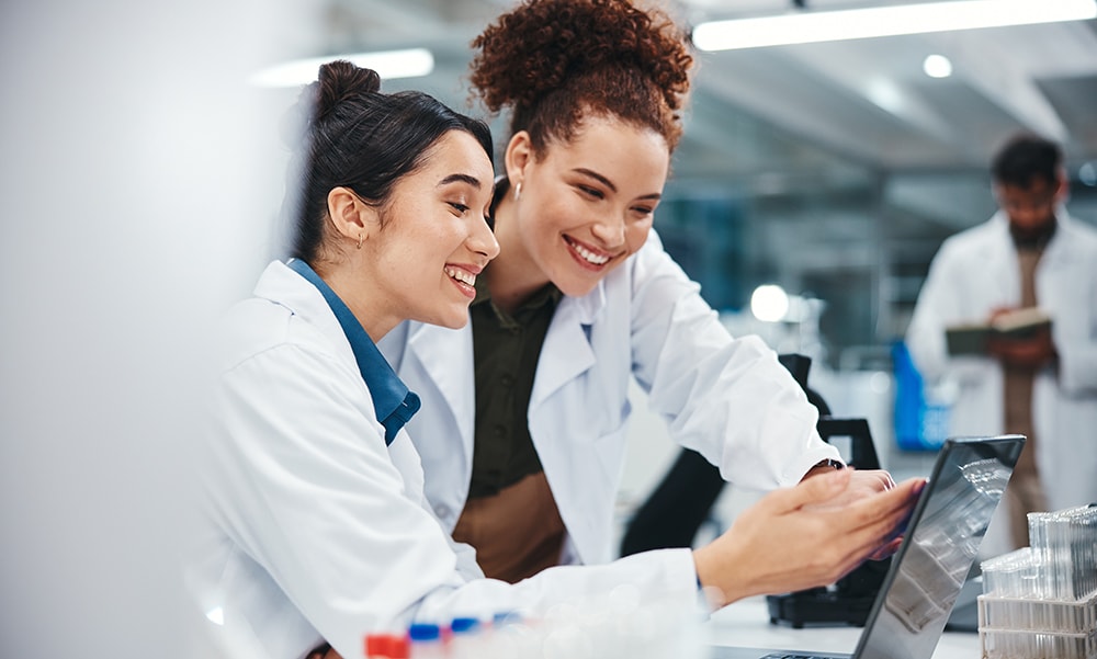 ordenador portátil, científico y mujeres sonrientes, investigación médica y expectación por los resultados de las pruebas y señalando. laboratorio, en línea y conversación sobre medicina y asistencia sanitaria, sector farmacéutico y colaboración