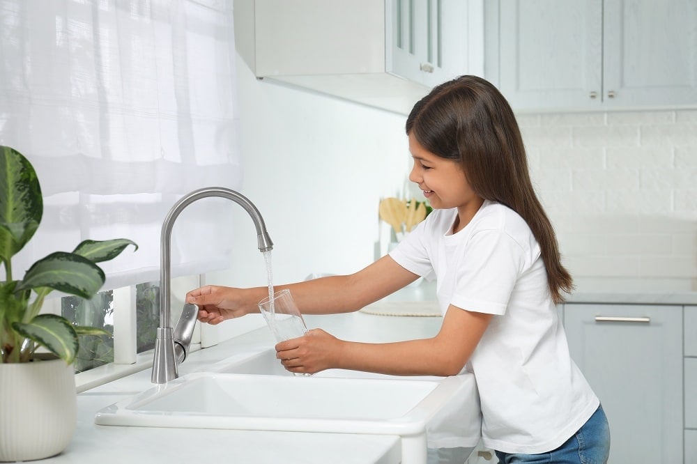 girl filling glass with water from tap in kitchen