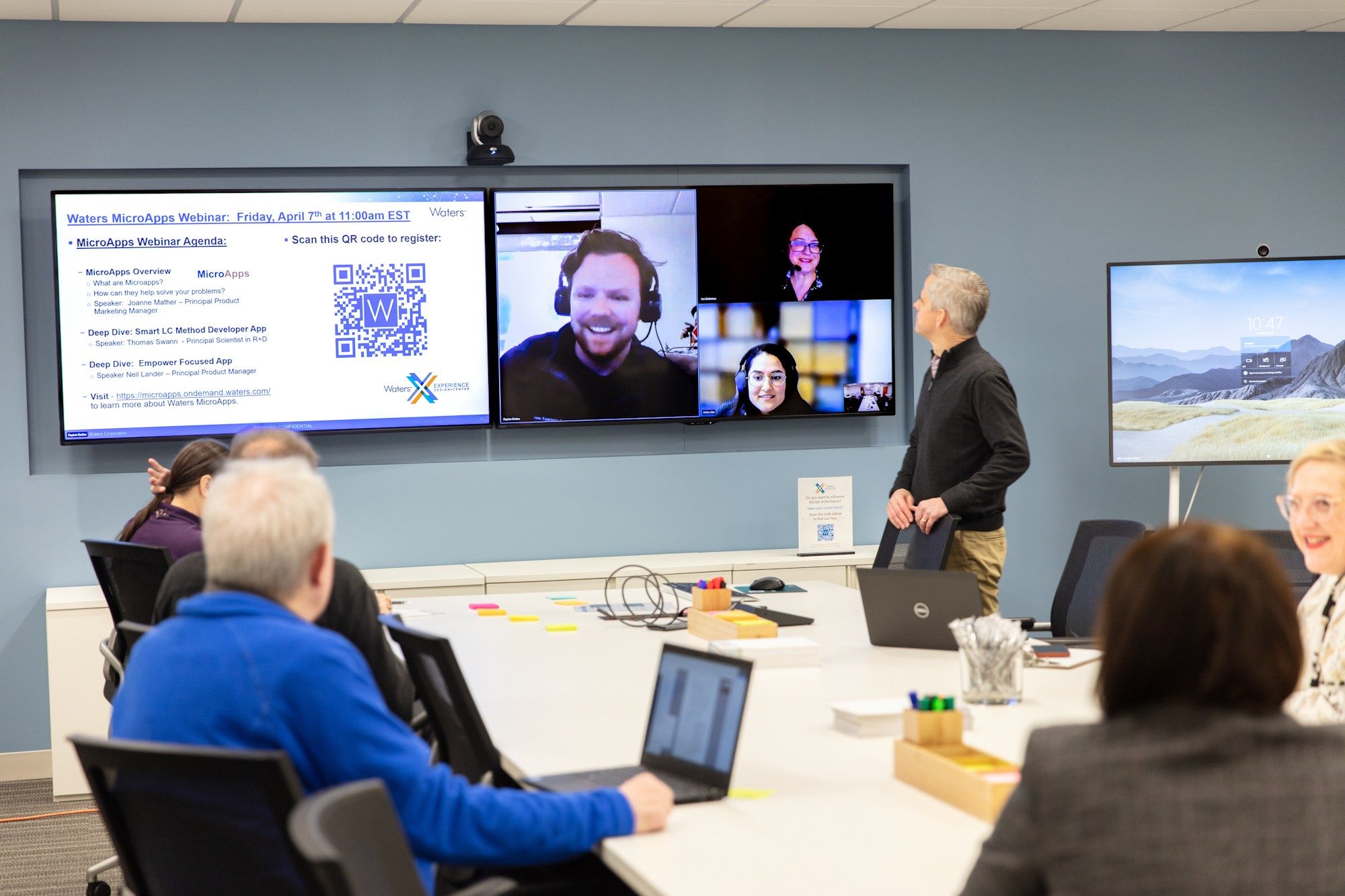 Researchers sit around a long table in the Observation Room while speaking with participants on a pair of monitors attached to the wall.
