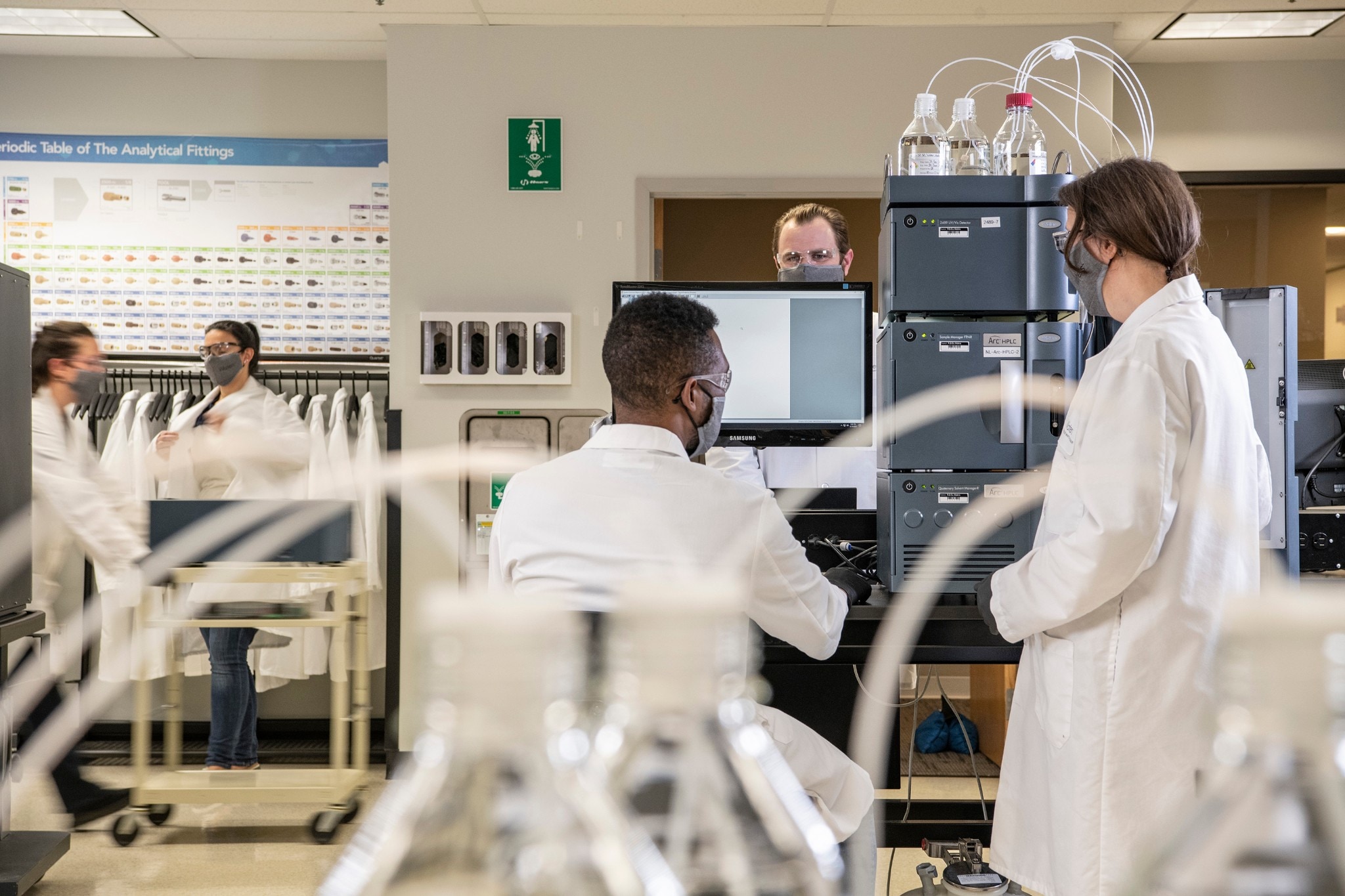 Five scientists wearing masks, working in a busy laboratory with an Arc HPLC system