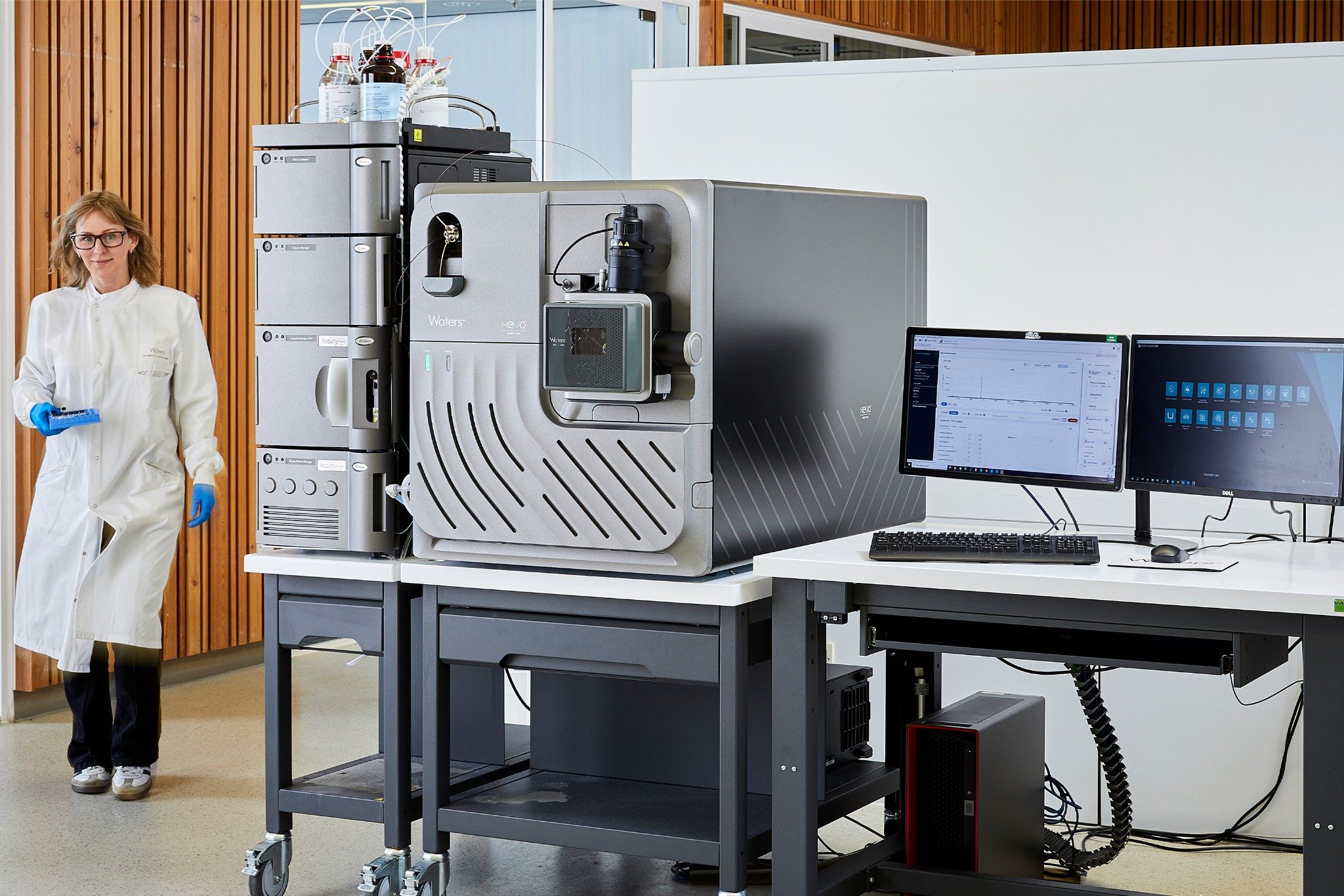 Scientist walking with well plate in laboratory near a Xevo MRT P10 system