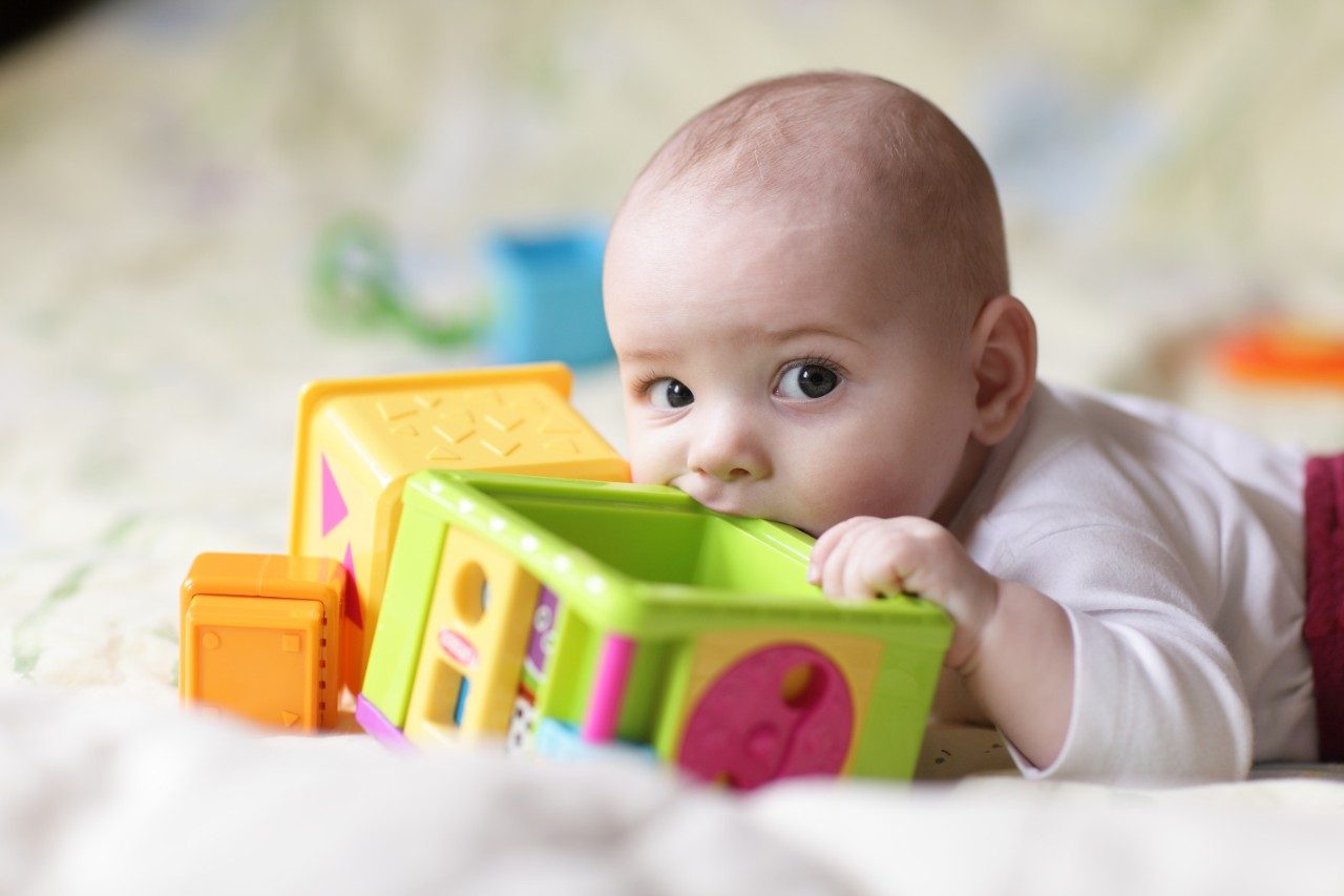 The baby boy bites toy block on a bed at home