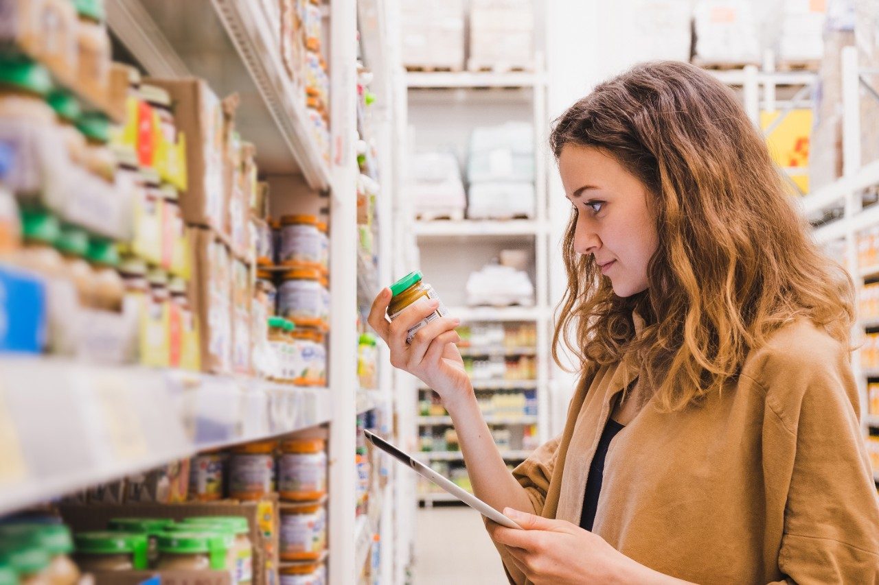 Woman with tablet reading baby food in a supermarket