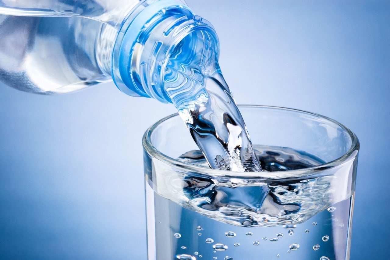 Pouring water from bottle into glass on blue background