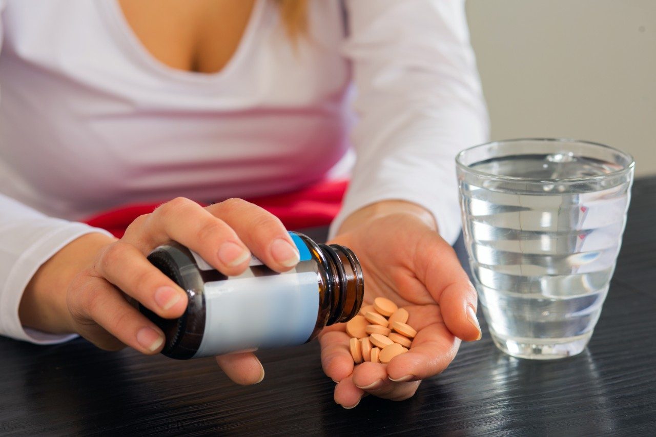 Pouring pills in hand with glass of water