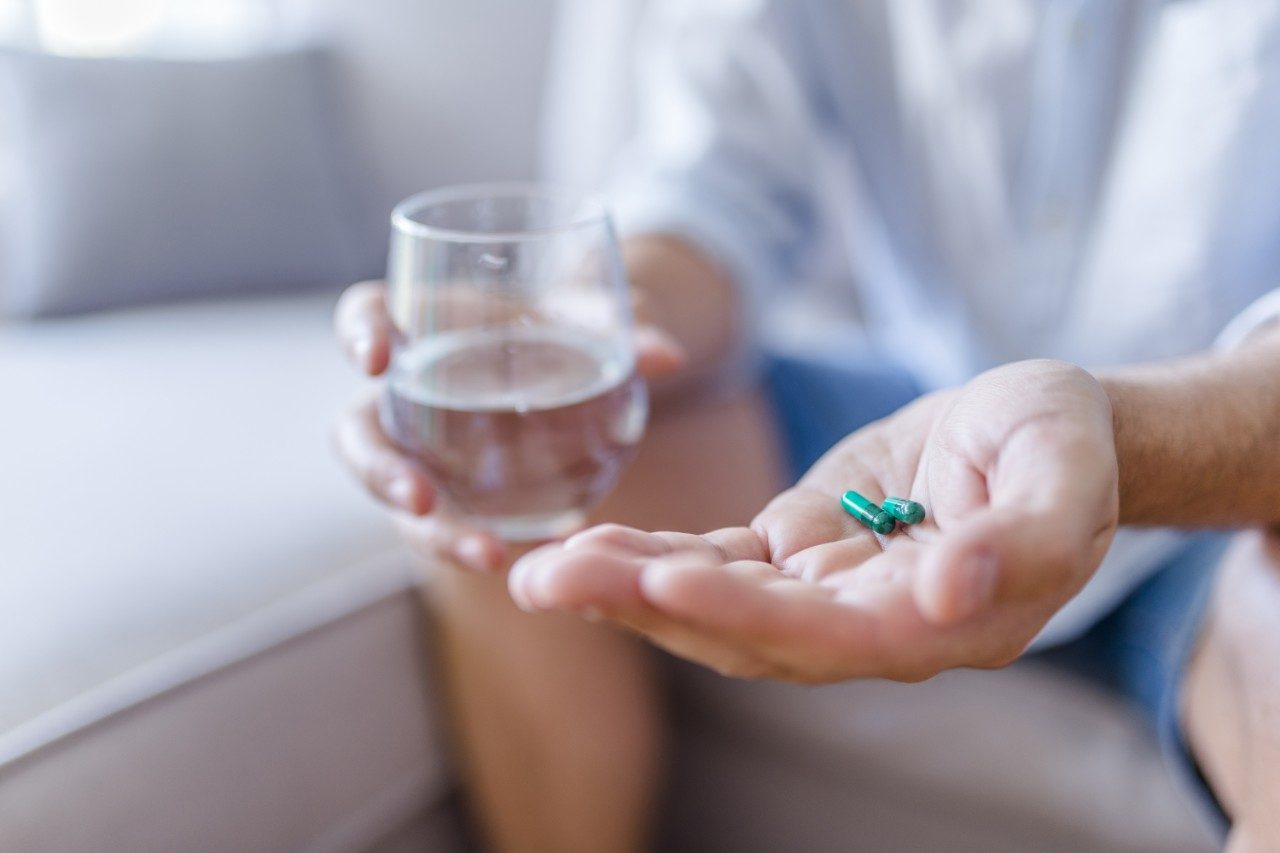Healthcare and medical concept. Close-up view of man holding pill in one hand and glass of water in the another hand. Focus on the pill