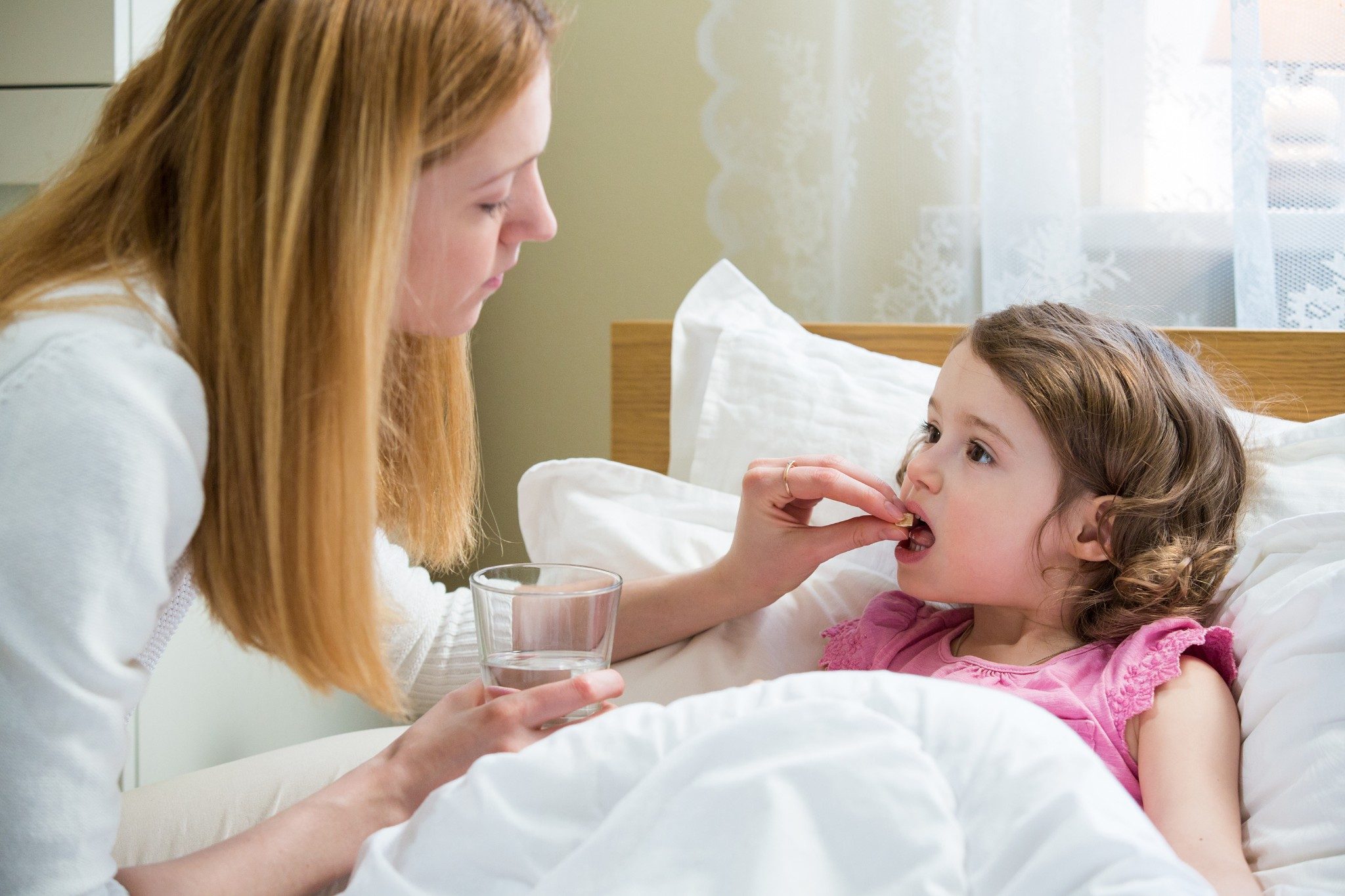 Mother giving glass of water and medicine to her ill child