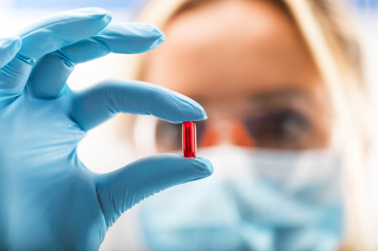 Scientist in PPE holding a red transparent pill