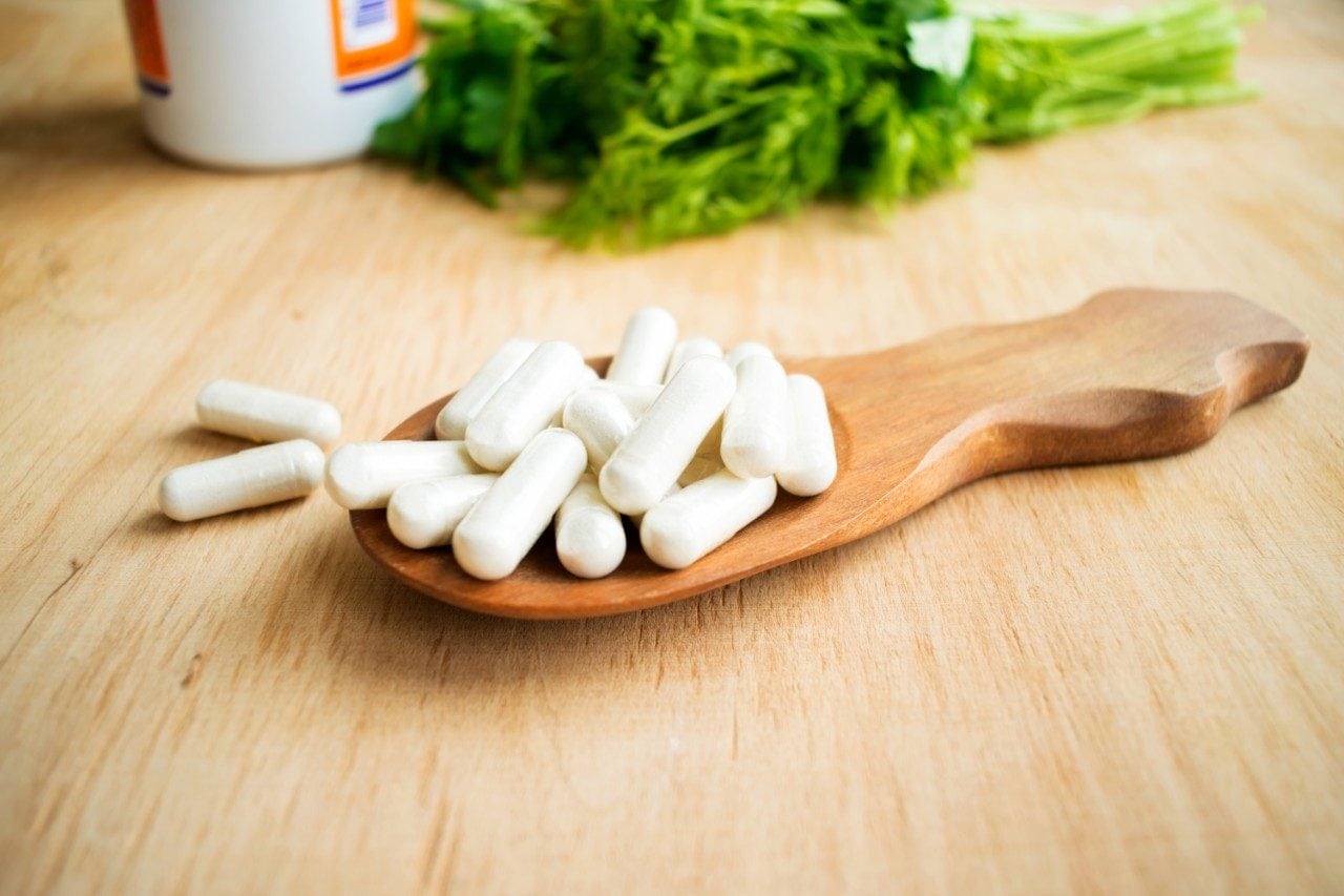 Vitamin K in wooden spoon with bottle of tablets and green herbs