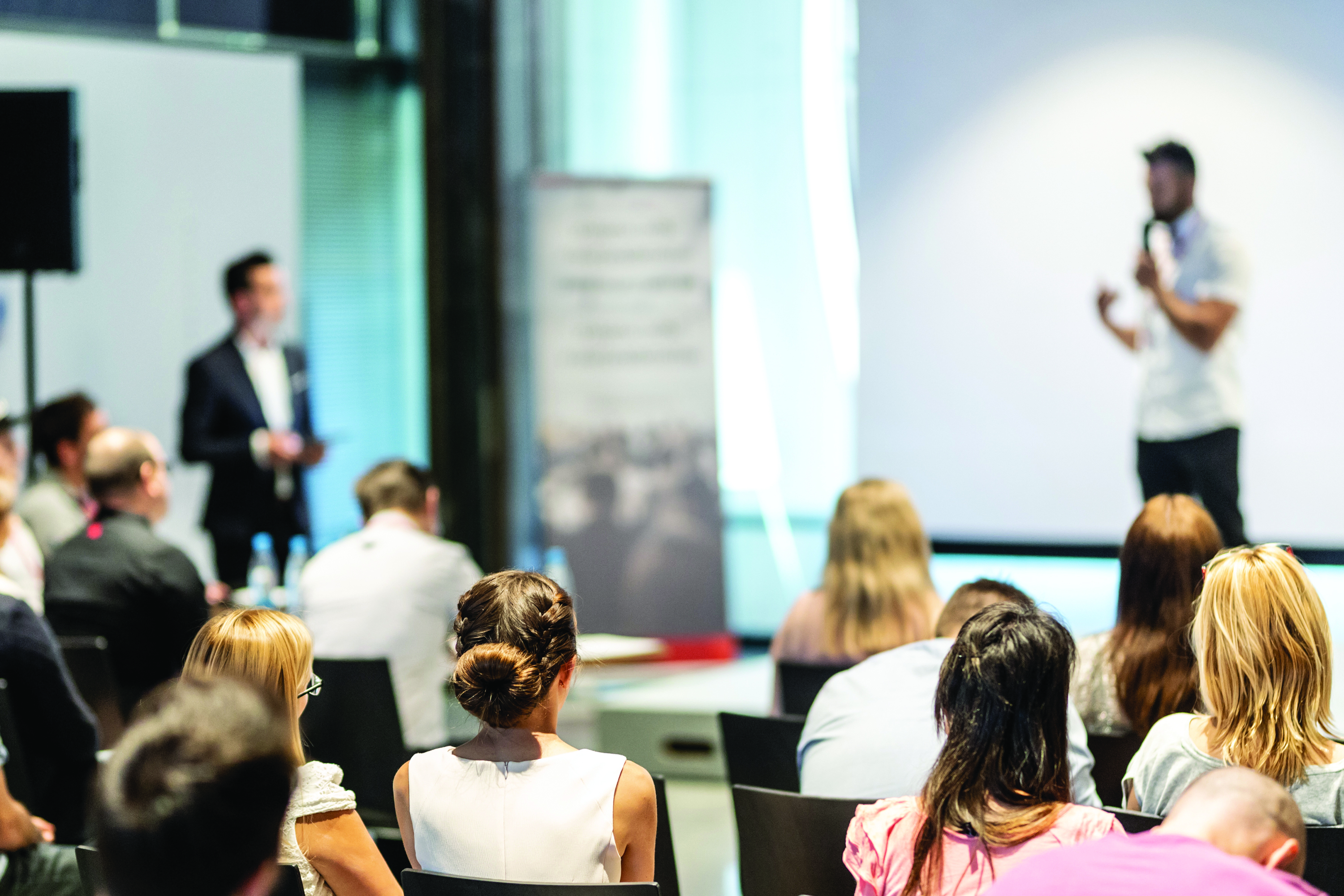 Two speakers on stage at a corporate event in front of an audience